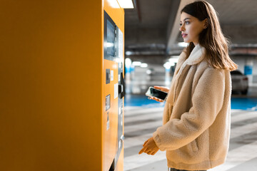 Elegant young girl pays for ticket in parking meter. Woman near terminal in the underground parking