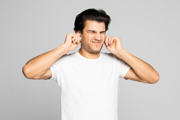 Fototapeta na wymiar I need silence. Frustrated young man in shirt and tie covering ears with hands and keeping eyes closed while standing against grey background