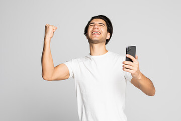 Portrait of a happy satisfied man looking at mobile phone and shouting iover white background