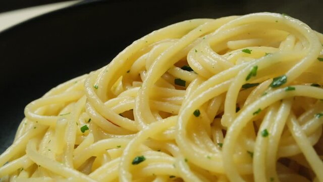 Delicious food pasta hot spaghetti with olive oil and parsley in a black plate. slow motion, rotation. Italian cuisine recipe