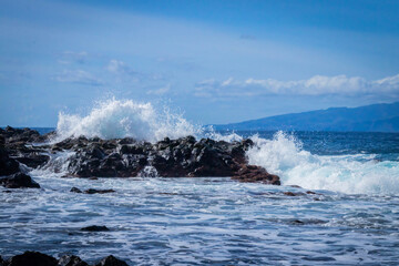 
turquoise ocean breaking waves against black beach and black rocks on a beautiful sunny day