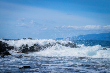 
turquoise ocean breaking waves against black beach and black rocks on a beautiful sunny day