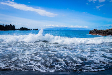 
turquoise ocean breaking waves against black beach and black rocks on a beautiful sunny day