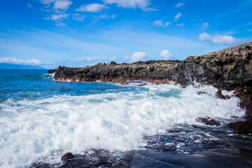Obraz premium turquoise ocean breaking waves against black beach and black rocks on a beautiful sunny day