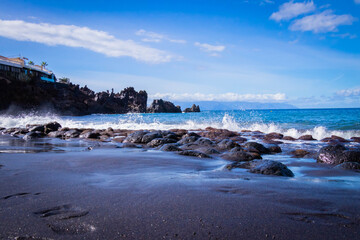 
turquoise ocean breaking waves against black beach and black rocks on a beautiful sunny day