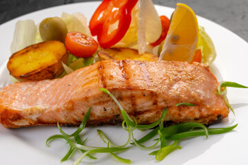 salmon steak with baked and fresh vegetables on a white plate and dark background. Grilled seafood. For the restaurant menu