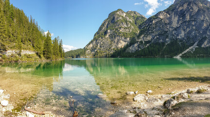 A panoramic view on the Pragser Wildsee, a lake in South Tyrolean Dolomites. High mountain chains around the lake. The sky and mountains are reflecting in the lake. Dense forest at the shore. Serenity
