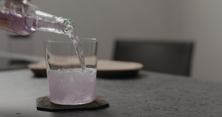 pour purple fizzy drink in a tumbler glass on concrete countertop with pasta on background