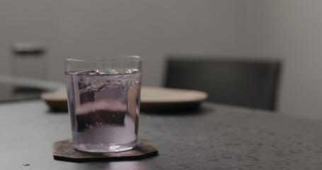 purple fizzy drink in a tumbler glass from concrete countertop with pasta on background