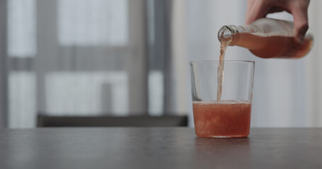 pour pink fizzy drink in a tumbler glass on concrete countertop with window on background