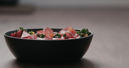 salad with kale, coppa and cherry tomatoes from black bowl on concrete countertop