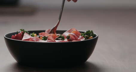 pick salad with kale, coppa and cherry tomatoes from black bowl on concrete countertop