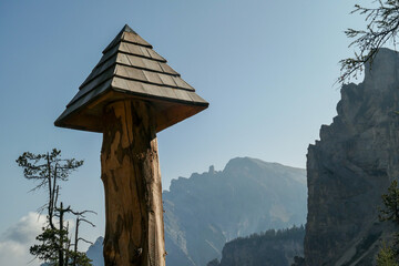 A close up view on a wooden rooftop placed on a wooden spike along a way in Italian Dolomites. Small decor. In the back there are high Italian Dolomites chains. Clear and sunny day.
