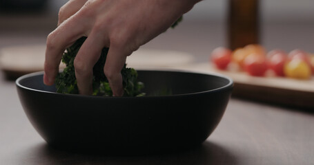 man making salad with kale, and cherry tomatoes in black bowl on concrete countertop