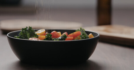 seasoning salad with kale, and cherry tomatoes in black bowl on concrete countertop