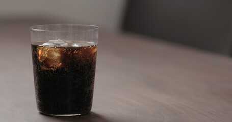 cola in tumbler glass with ice on walnut table with copy space
