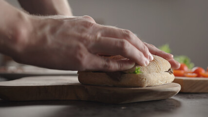 Obraz na płótnie Canvas Man put top bun on steak ciabatta sandwich on kitchen countertop