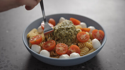 man eat pesto fusilli pasta with mozzarella and cherry tomatoes from blue bowl on concrete background