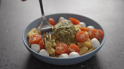 man eat pesto fusilli pasta with mozzarella and cherry tomatoes from blue bowl on concrete background