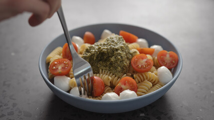 man eat pesto fusilli pasta with mozzarella and cherry tomatoes from blue bowl on concrete background
