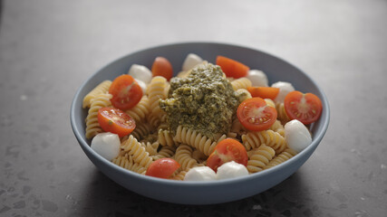 pesto fusilli pasta with mozzarella and cherry tomatoes from blue bowl on concrete background
