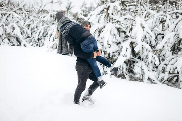 The guy holds the girl in his arms in the snowy winter forest