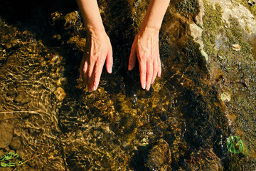 The girl traveler washes her hands in cold river water. Sun glare on clear natural mountain water. Woman unity with nature. Freshness splashing. Recreation in hot summer day