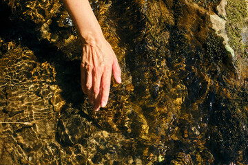 The girl traveler washes her hands in cold river water. Sun glare on clear natural mountain water. Woman unity with nature. Freshness splashing. Recreation in hot summer day