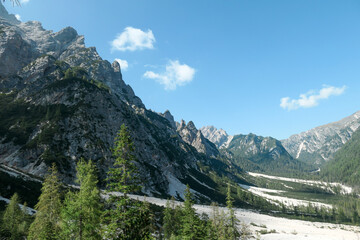 Fototapeta premium A massive landslide area in Italian Dolomites. The whole area is full of small stones and pebbles. In the back there are high and sharp mountain chains. Raw and desolated area. Few trees on the slopes