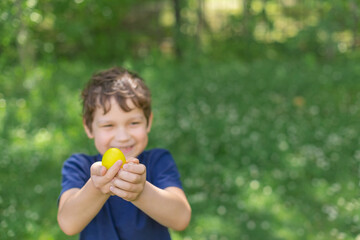 Easter yellow colored egg in boys hand in blooming spring garden. Preschooler boy plays outdoors, he is Easter egg hunt alone. Copy space.
