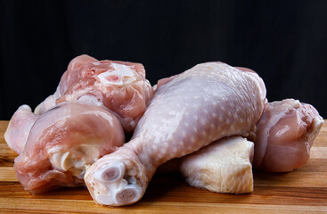 A bunch of raw chicken legs on a wooden board.a side view.