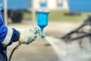 Spray gun in hand. A worker in overalls and a glove holds a spray compressor for painting in his...