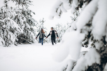 Fototapeta na wymiar Loving couple runs through a snowy forest in winter in a sweater and a scarf and smiles