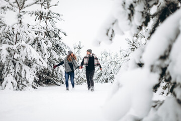 Loving couple runs through a snowy forest in winter in a sweater and a scarf and smiles