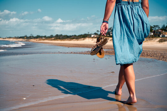 A barefoot female walking on the seashore, backshot of the sun-tanned slim legs