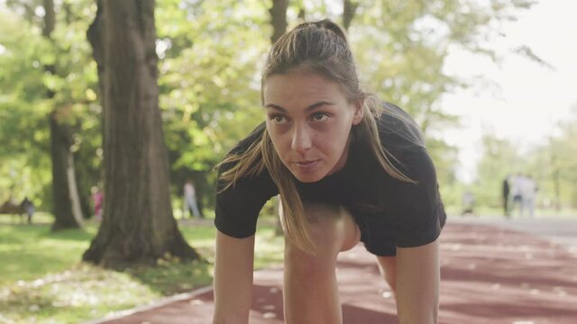 fitness girl exercising on an all weather synthetic track surface in the park, starting position for running