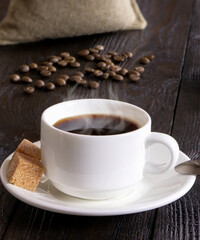 A cup of coffee on a wooden background. Morning hot coffee on a wooden table. Coffee beans. A white coffee cup and cane sugar. Steam.Espresso. Vertical orientation