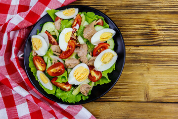 Tasty tuna salad with eggs, lettuce and fresh vegetables on wooden table. Top view