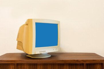CRT old computer monitor blue screen on wooden table in front of white wall in the house, with copy space on the light