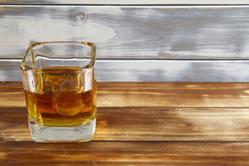 Close up of one isolated whisky glass with ice cube and timber wood planks background, copy space for text (focus on glass)