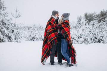 Fototapeta na wymiar Couple in love hiding with a blanket in a snowy beautiful winter forest