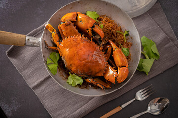 Baked fresh sea crab with vermicelli or glass noodle in the cook pot with table set up ready to eat. Black background © Super Happy Nerd