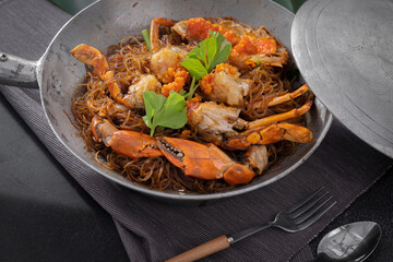 Baked fresh sea crab with vermicelli or glass noodle in the cook pot with table set up ready to eat. Black background