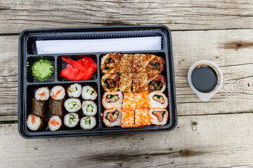 Set of sushi rolls in plastic box on wooden table. Sushi for take away or delivery of sushi in plastic container. Top view