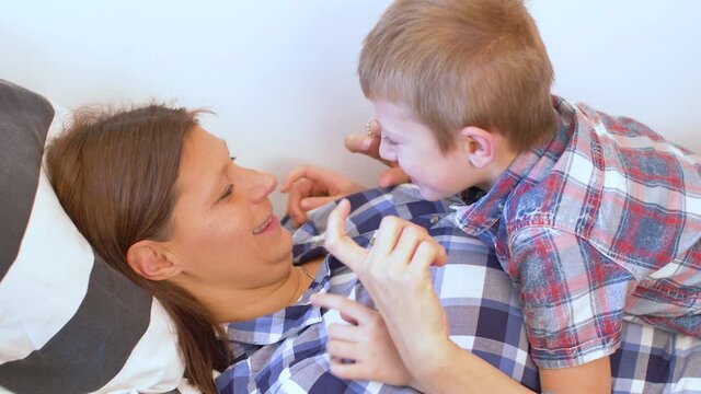 young mom and her son are cuddled and tickled on the sofa at home