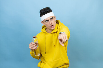 Young caucasian man wearing sportswear holding water bottle over isolated blue background pointing with finger surprised ahead, open mouth amazed expression, something on the front