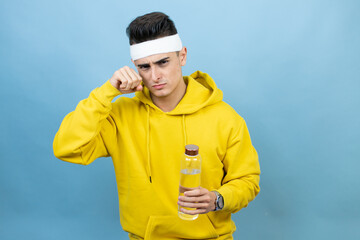 Young caucasian man wearing sportswear holding water bottle over isolated blue background depressed and worry for distress, crying angry and afraid. Sad expression.