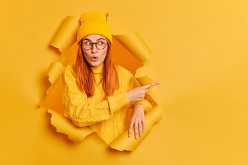 Pretty redhead gir with wondered expression indicates at blank space says wow looks at this promo...