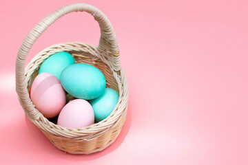 Easter decor: colored eggs in a basket, pink background. Preparing for Easter. The photo