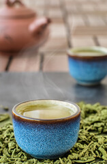 Hot green tea in a blue tea bowl, stone table. Steam rises from the bowl. Tea leaves next to the cup. Close-up, tea ceremony. Minimal